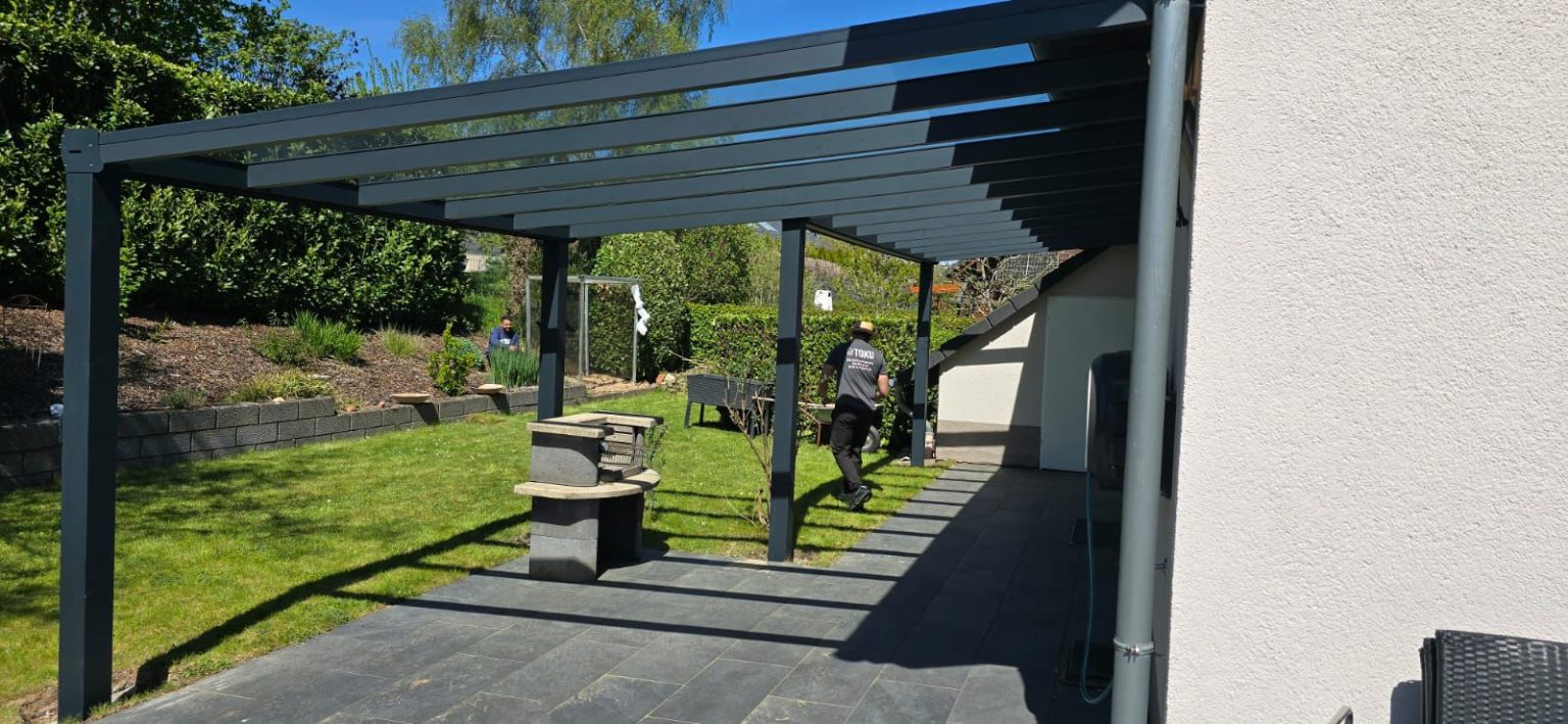 Terrassenüberdachung aus Aluminium mit Glasdach im Garten – montiert von Toku Bauelemente